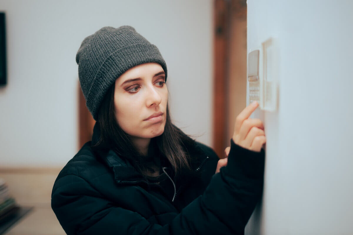 Woman feeling cold at home checking thermostat
